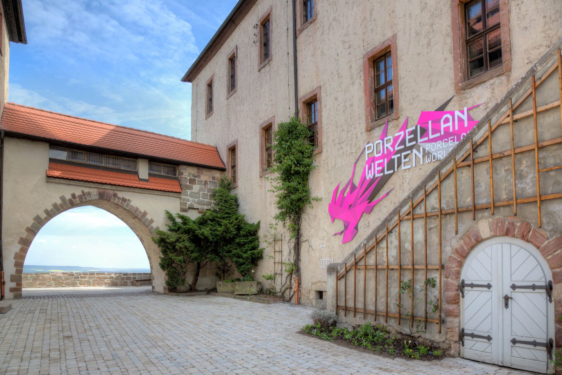 weißer Schriftzug „Porzellanwelten” auf Leitsymbol in kräftigem Magenta