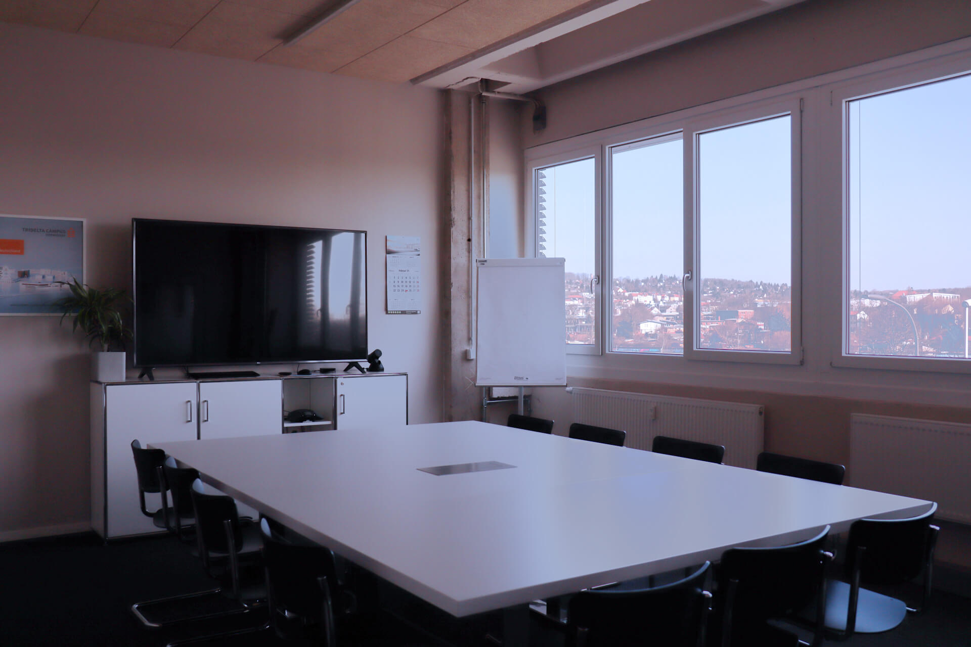 Modern ausgestatteter Konferenzraum mit großem Tisch und TV, Fensterblick auf Gera